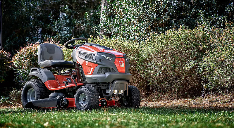 Red and black riding lawn mower parked on neatly cut grass next to row of shrubs