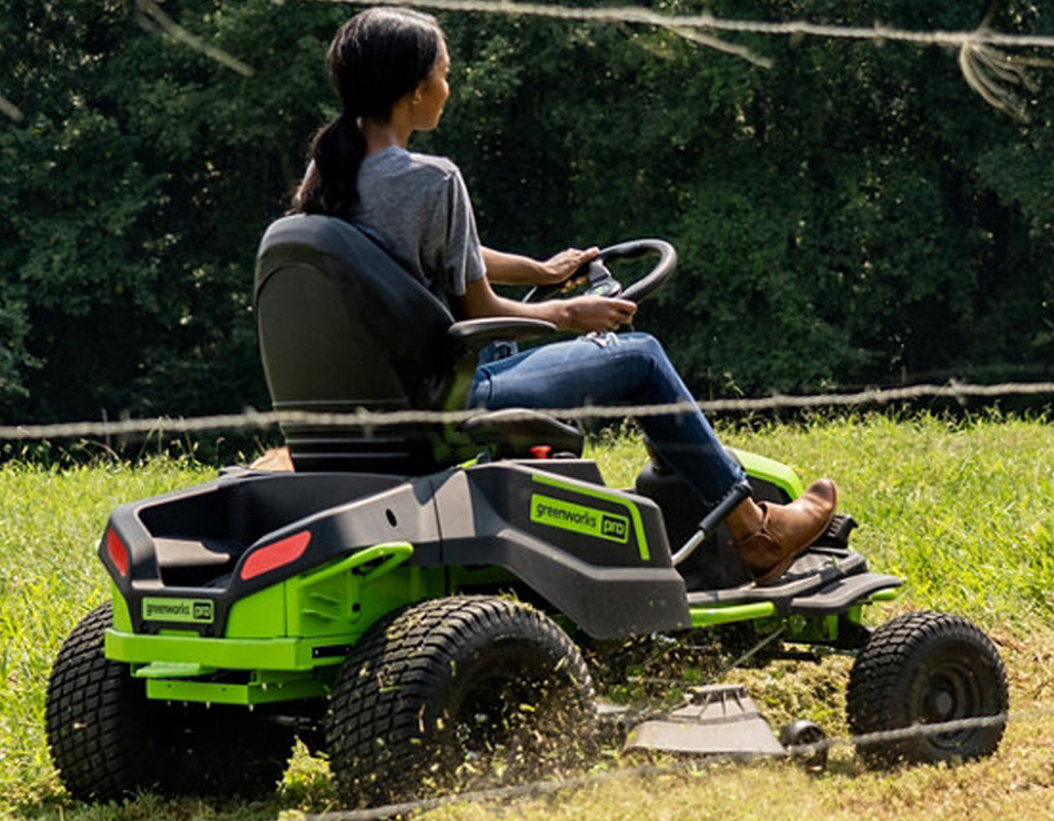 Person using electric riding mower to cut grass along wire fence