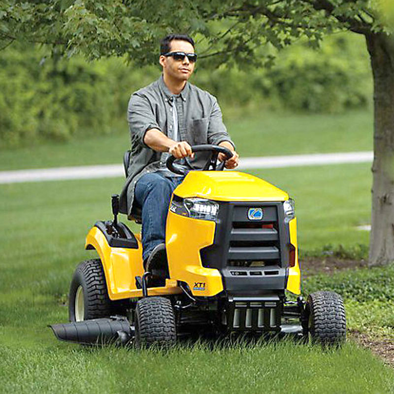 Person using yellow riding mower to cut grass long garden bed