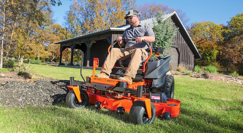 Homeowner uses orange Bad Boy zero-turn riding mower to cut grass around garden bed