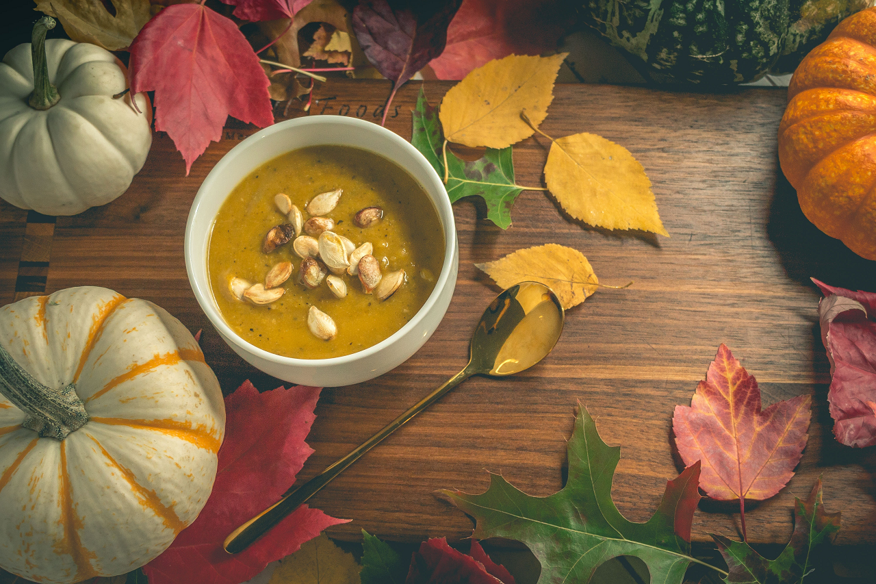 Image of a bowl of pumpkin soup next to white pumpkins.